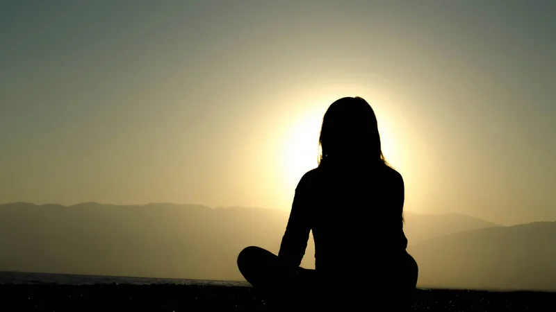 Personne assise en méditation face au lever du soleil sur l’eau